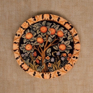 May include: Circular wall art depicting a tree laden with orange fruit, green foliage, and a black backdrop. The artwork is framed with a tan and orange floral border. The piece is likely made of fabric or a similar material.