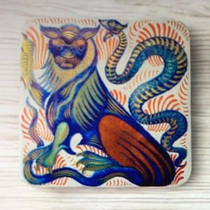 May include: Square coaster with a mythical creature design. The artwork depicts a blue and orange griffin-like figure with a long, serpentine tail. The background features orange and white stylized flame-like patterns.