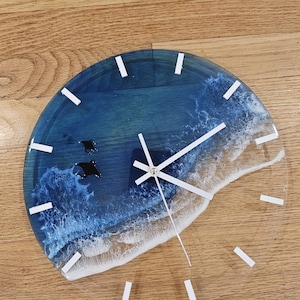 May include: A blue and white resin clock with a wave design and white clock hands. The clock face has white Roman numeral markings.