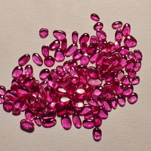 Peut inclure: Un grand groupe de pierres précieuses ovales roses, probablement des rubis, éparpillées sur une surface blanche.