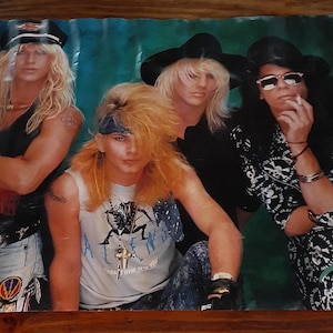 May include: A vintage poster featuring the rock band Poison. The image shows four band members in various poses, with long hair and rock-and-roll attire. The band's name is visible in a stylized font at the bottom right.