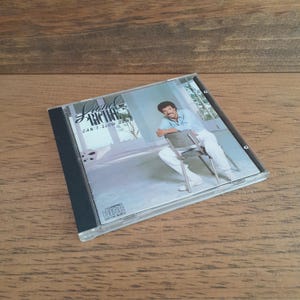 May include: A Lionel Richie Can't Slow Down music CD in a clear plastic jewel case. The cover art features a man in a light blue shirt and white trousers sitting on a metal chair. The Compact Disc Digital Audio logo is printed in the corner.