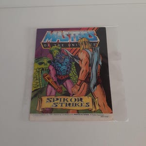 May include: A vintage Masters of the Universe comic book titled Spikor Strikes, featuring a colorful illustration of He-Man and the character Spikor in front of a green stone fortress. The cover includes the series logo and copyright text.