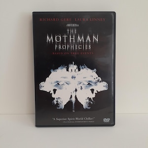 May include: A black DVD case for the film The Mothman Prophecies starring Richard Gere and Laura Linney. The cover features white inkblot-style artwork resembling a moth or face, with the title text and the phrase Based on True Events.