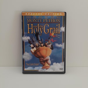 May include: A DVD case for the film Monty Python and the Holy Grail, Special Edition. The cover features a large golden chalice held by a hand, with several figures inside against a blue sky with clouds, and the film title in yellow text.