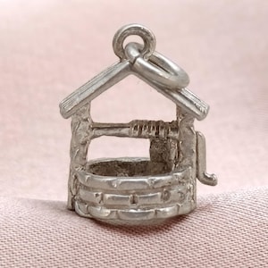 Può includere: Un piccolo ciondolo color argento a forma di pozzo dei desideri. Il ciondolo presenta una base a forma di mattoni, un piccolo tetto e una manovella. È progettato per essere attaccato a un braccialetto o una collana.