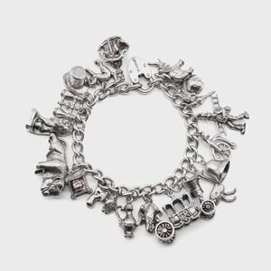 May include: A silver charm bracelet with various detailed charms. Charms include a top hat, a wizard hat, a carriage, a bell, a heart, a firefighter, and a lock. The bracelet is made of linked chain.