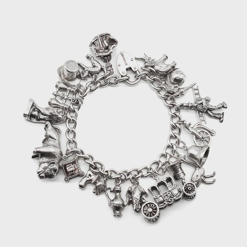 May include: A silver charm bracelet with various detailed charms. Charms include a top hat, a wizard hat, a carriage, a bell, a heart, a firefighter, and a lock. The bracelet is made of linked chain.