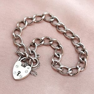 May include: A silver chain bracelet with a heart-shaped padlock charm. The chain is a curb link style.