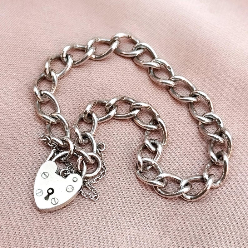 May include: A silver chain bracelet with a heart-shaped padlock charm. The chain is a curb link style.