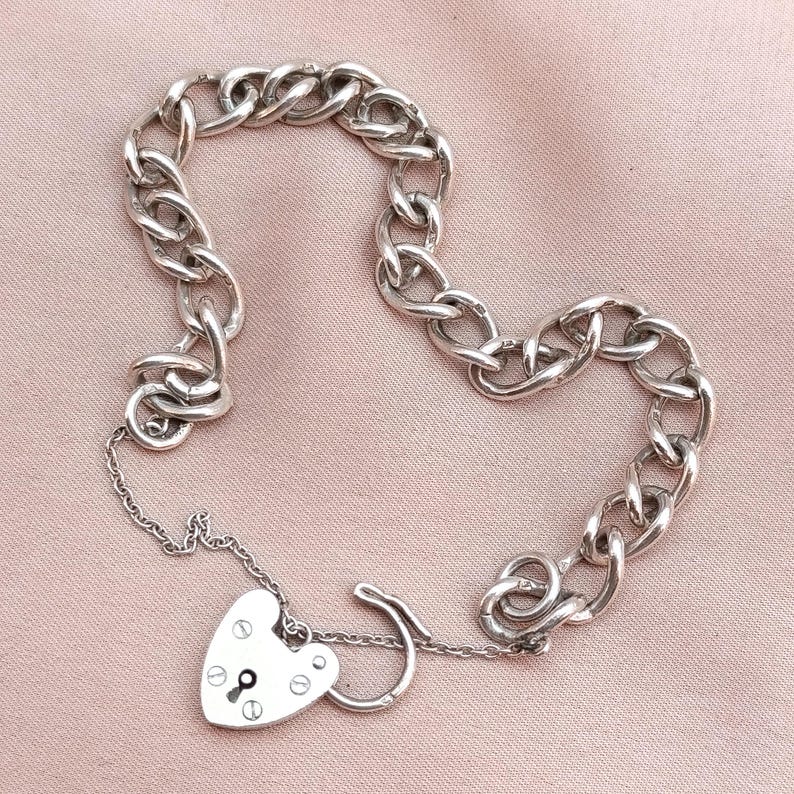 May include: A silver chain bracelet with a heart-shaped padlock charm. The chain is made of interlocking links and the padlock has a keyhole.