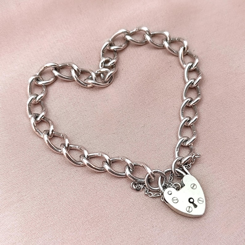 May include: A silver chain bracelet with a heart-shaped padlock charm. The chain is a curb style and the padlock has a keyhole and a small screw detail.