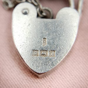 May include: Close-up of a silver heart-shaped padlock with a chain. The padlock has hallmarks including a crown, a lion, and a letter 'T'.