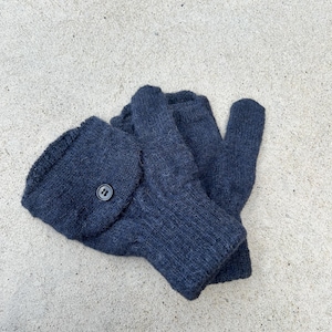 May include: A pair of dark blue knitted convertible mittens with a button closure. The mittens can be worn as fingerless gloves or as mittens. The knitted texture is visible, and the mittens are lying on a concrete surface.