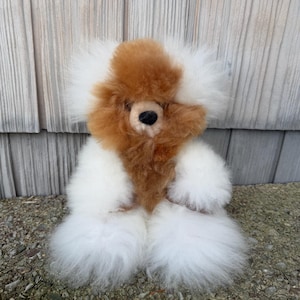 May include: A plush teddy bear toy featuring long, fluffy white fur on its body and limbs, with a distinct patch of brown fur covering its face and chest. The bear has a small, round black nose and dark eyes nestled within the thick, soft texture.