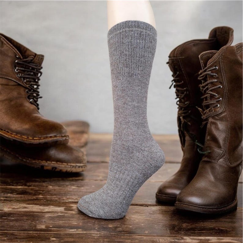 May include: A pair of gray crew socks with a ribbed texture. The socks are shown on a model's leg with brown leather boots in the background.