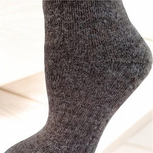 May include: A close-up of a gray sock made of a soft, textured fabric. The sock is shown on a white surface.