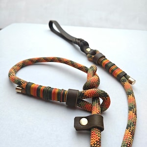 Könnte beinhalten: Ein Hundeleinen- und passendes Halsband-Set. Die Leine hat einen dunkelbraunen Ledergriff und Akzente mit einem farbenfrohen Seildesign in Orange, Grün und Gelb. Das Halsband hat ein ähnliches Seildesign und Lederakzente.