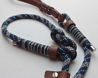 May include: A blue and white patterned dog leash with brown leather accents. The leash features a loop handle and a metal clasp. The design includes a series of knots and leather details.