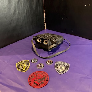 May include: A black night vision device with a strap and five circular or shield-shaped patches. The patches feature text including 501st Legion, Special Ops, Swift, Silent, and Relentless, along with graphic designs of dragons and military-style emblems.