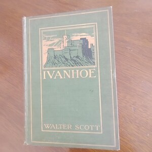 May include: A vintage hardcover book titled "Ivanhoe" by Walter Scott. The book has a green cover with gold lettering and a castle illustration. The book is resting on a wooden surface.