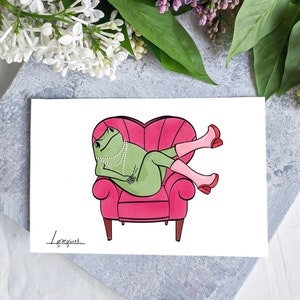 May include: A green frog wearing a pearl necklace and pink shoes sits in a pink heart-shaped armchair. The frog is looking to the left of the image.