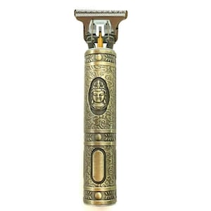 Könnte beinhalten: Goldener elektrischer Haarschneider mit einem detaillierten Design mit einem Buddha-Kopf und komplizierten Mustern. Der Haarschneider hat eine goldfarbene Klinge und einen schwarzen Schalter.