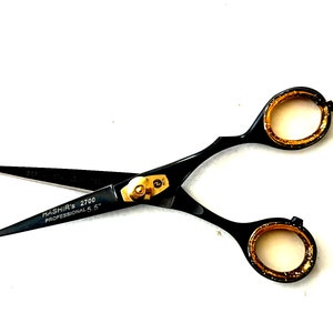 May include: Black hairdressing shears with gold accents. The shears have a 5.5 inch blade and are labeled "HASHIR'S 2700 PROFESSIONAL 5.5*"