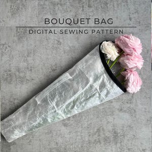 Peut inclure: Un sac à bouquet blanc avec une bordure noire. Le sac est fait d'un matériau léger et translucide et est conçu pour contenir un bouquet de fleurs. Le sac est plié et posé sur une surface texturée grise. Le texte "BOUQUET BAG DIGITAL SEWING PATTERN" est imprimé sur la surface.