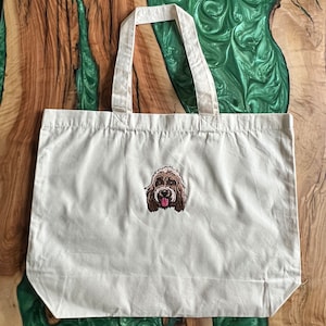 May include: A white canvas tote bag with a brown and white embroidered dog face on the front.