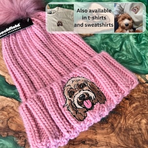 May include: Pink knitted beanie with a fluffy pom pom on top and an embroidered dog face. The beanie is also available in t-shirts and sweatshirts.
