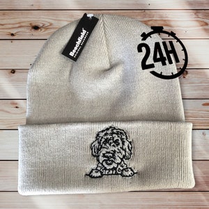 May include: A beige knitted beanie with a black embroidered dog on the front. The beanie has a fold-over cuff and a tag that says "Beechfield Original Headwear".