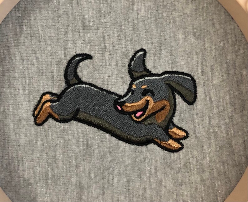 May include: Embroidered patch of a black and brown dachshund running with a happy expression. The patch is on a gray background.