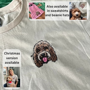 May include: A light beige t-shirt featuring an embroidered dog portrait. The dog has brown fur, a pink tongue, and a black nose. The text "Christmas version available" is printed below the dog. The text "Also available in sweatshirts and beanie hats" is printed in the top right corner.