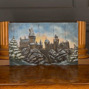 May include: A painting depicting a castle with multiple towers and turrets, covered in snow, set against a cloudy sky with orange hues. The artwork features detailed architecture and snowy pine trees, creating a winter scene.