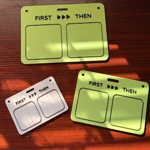 May include: Two lime green and one white rectangular visual schedule boards featuring the text FIRST, three arrow icons, and THEN. Each board includes two square recessed areas for placing cards, with holes at the top for hanging or attachment.