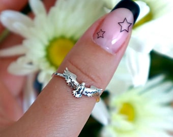 May include: A silver-toned metal ring featuring a detailed bird with outstretched wings. The bird is positioned centrally on the thin, polished band, showcasing engraved feather textures across the wings and body of the avian design.