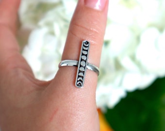 May include: A silver ring with a vertical bar design featuring a series of crescent moons.