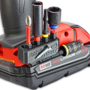 Pode incluir: Um suporte de pontas preto impresso em 3D com a etiqueta DIY RABBIT, fixado a uma bateria vermelha e preta M18 REDLITHIUM CP 2.0. O suporte contém quatro pontas metálicas e um adaptador, com um parafuso prateado numa ranhura horizontal.