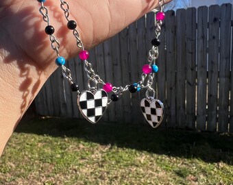 May include: A silver chain necklace with black and turquoise beads and pink accents. The necklace has two checkerboard heart pendants.