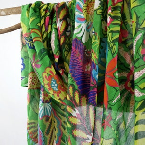 Puede incluir: Una bufanda verde transparente con un estampado floral colorido. El estampado presenta flores de color rosa, amarillo, azul y rojo brillantes sobre un fondo verde.