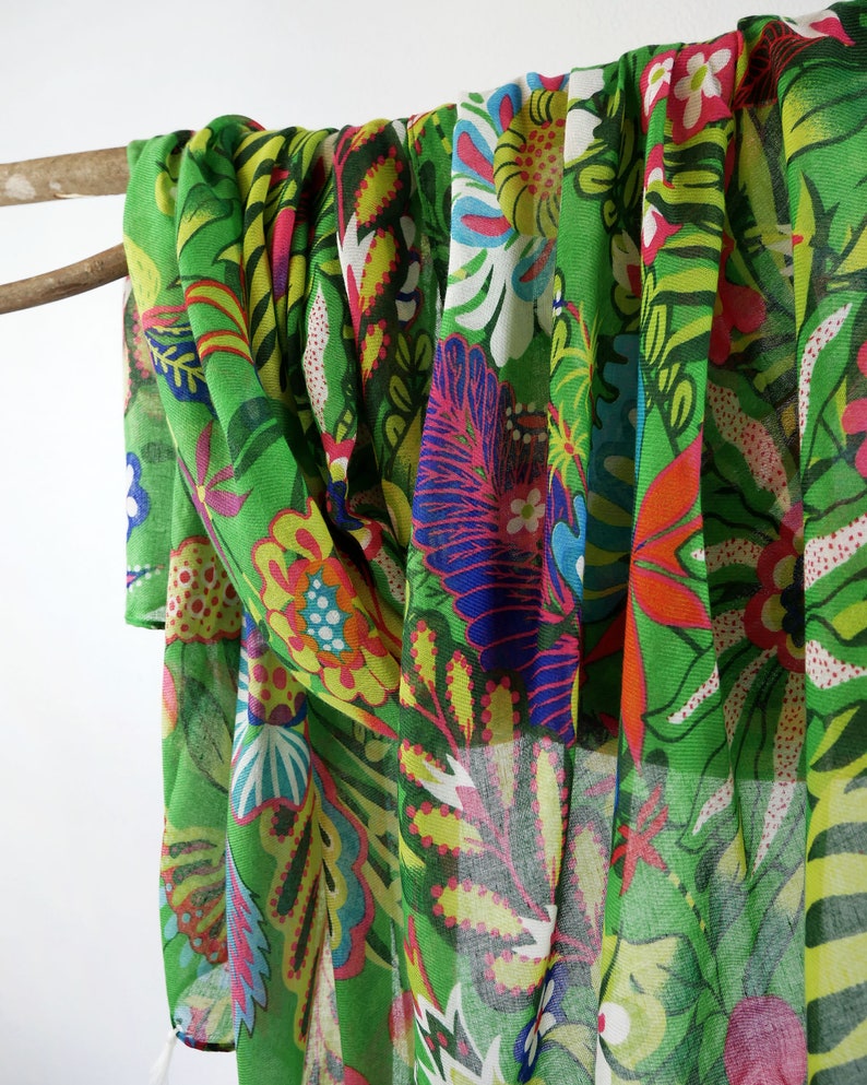 Puede incluir: Una bufanda verde transparente con un estampado floral colorido. El estampado presenta flores de color rosa, amarillo, azul y rojo brillantes sobre un fondo verde.