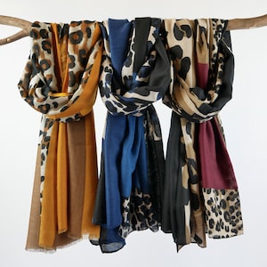 May include: Three scarves with a leopard print pattern. The scarves are in different color combinations: mustard yellow and brown, blue and black, and black and burgundy.