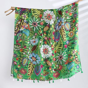Puede incluir: Una bufanda verde con un estampado floral colorido. La bufanda tiene un borde de flecos y est&aacute; hecha de una tela ligera.