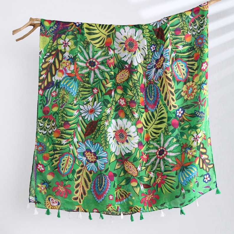 Puede incluir: Una bufanda verde con un estampado floral colorido. La bufanda tiene un borde de flecos y est&aacute; hecha de una tela ligera.