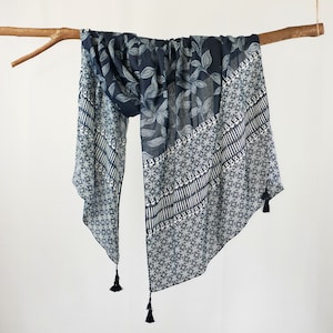 May include: A black and white patterned scarf with tassels. The scarf features a leaf design on one side and a geometric pattern on the other.
