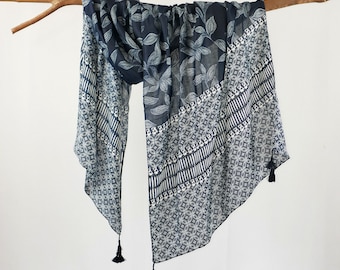 May include: A black and white patterned scarf with tassels. The scarf has a leaf design on one side and a geometric pattern on the other.