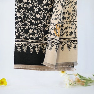 May include: A black and beige patterned scarf with a fringe border. The scarf has a small embroidered letter "B" on the beige side.