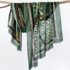 May include: A green scarf with a geometric pattern and a floral design. The scarf has a fringed edge.