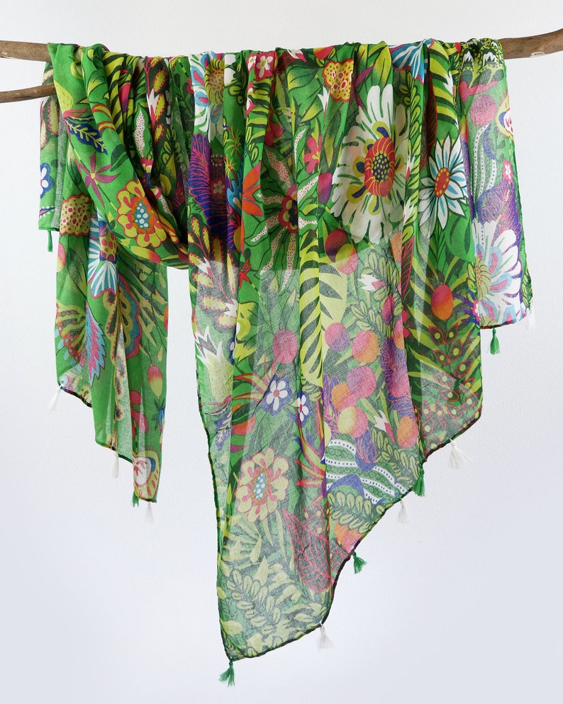 Puede incluir: Una bufanda de gasa verde con estampado floral de colores. La bufanda tiene borlas en los extremos.